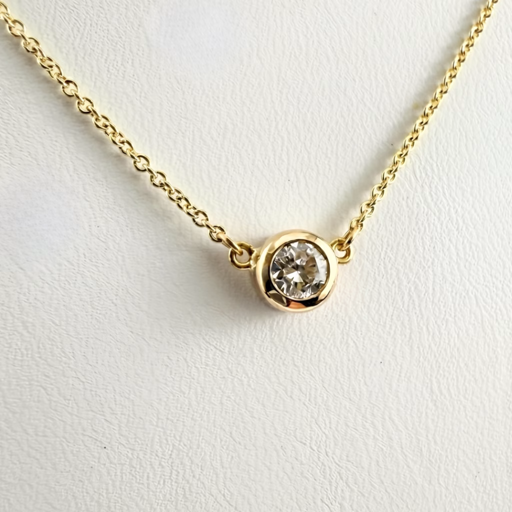 A delicate gold chain necklace featuring a single round brilliant-cut diamond pendant securely held in a polished bezel setting.