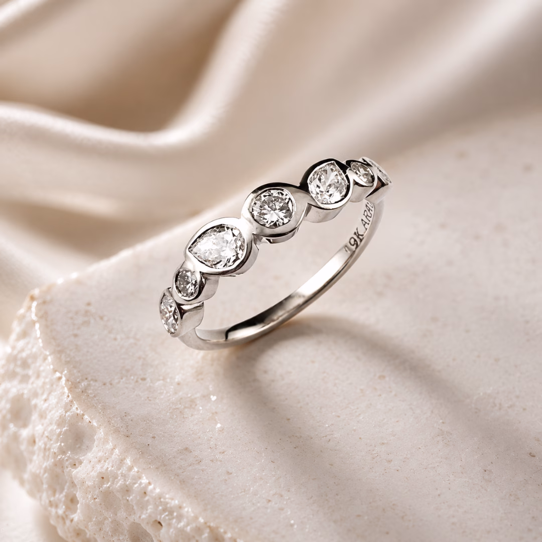 White gold diamond band featuring mixed diamond shapes in bezel settings styled on draped champagne-toned fabric.