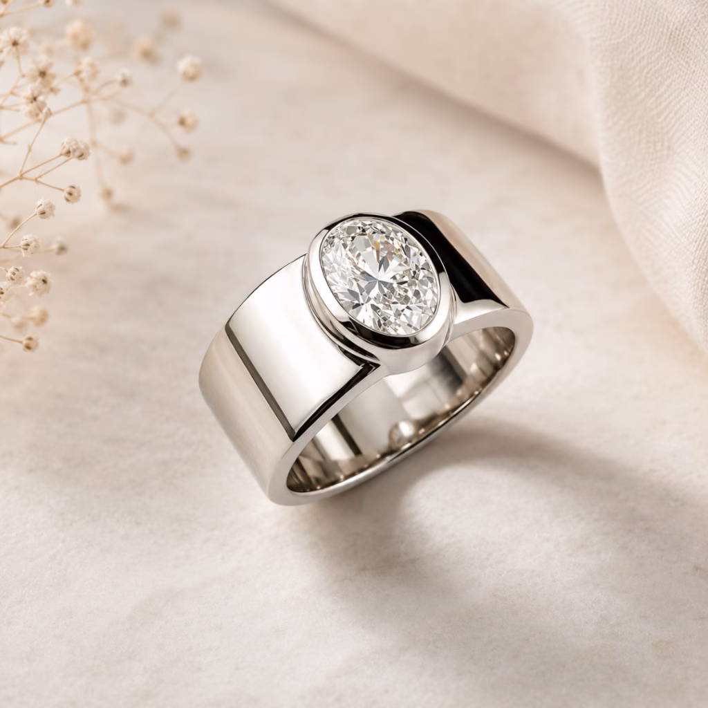Wide silver bezel-set diamond ring photographed on a warm neutral luxury jewellery background.