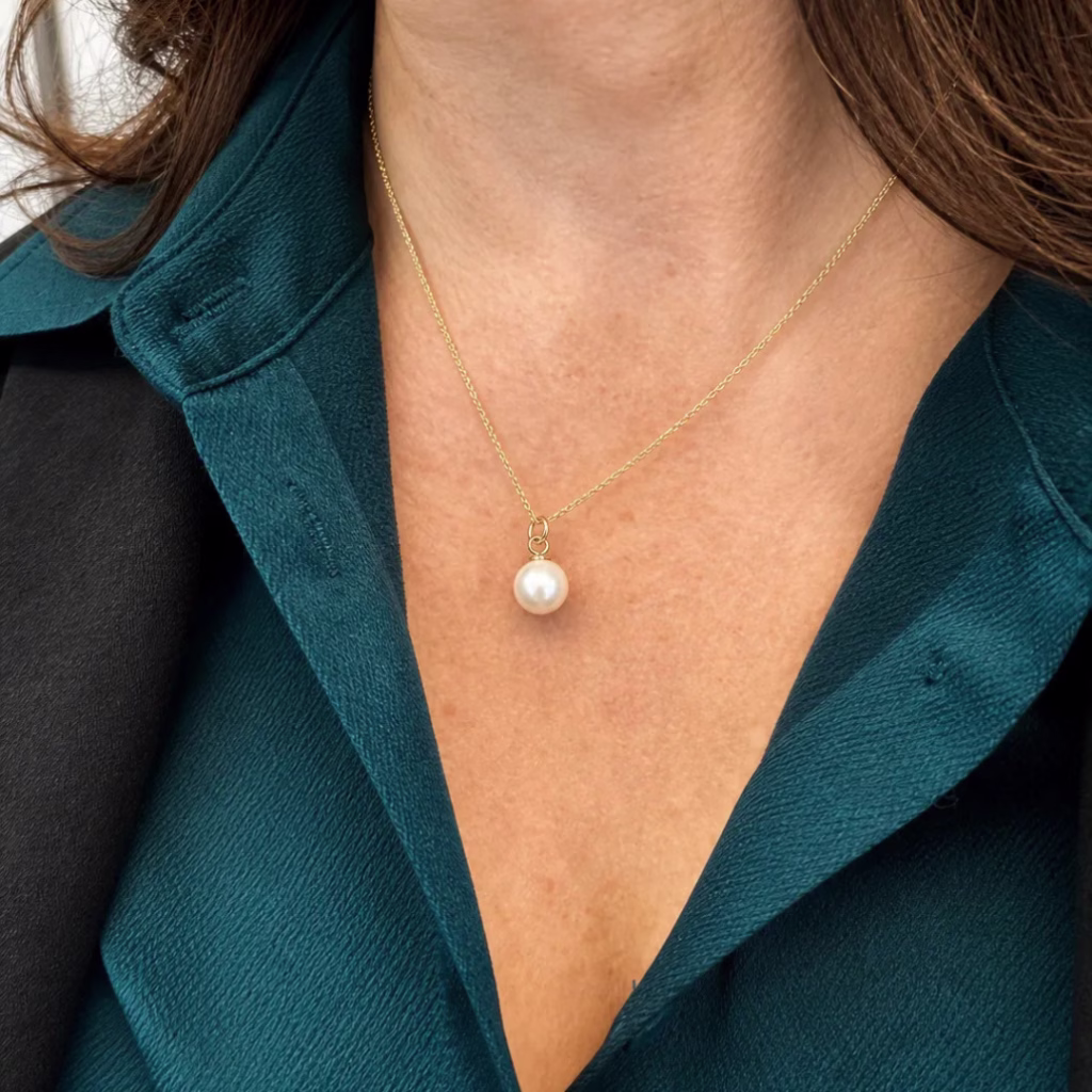 Close-up of a single pearl pendant on a fine gold chain.